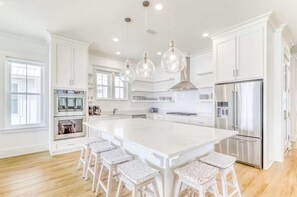 A modern kitchen with a large island, white cabinetry, stainless steel appliances, and pendant lighting. - Beach Vista One Beach House (Orange Beach)