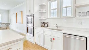 A modern kitchen with white cabinetry, a stainless steel dishwasher, and a window above the sink. - Beach Vista One Beach House (Orange Beach)