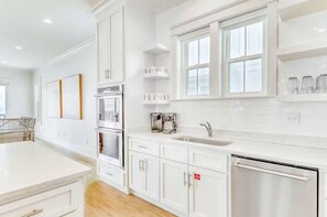 A modern kitchen with white cabinetry, a stainless steel dishwasher, and a window above the sink. - Beach Vista One Beach House (Orange Beach)