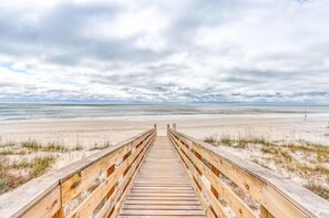 A wooden boardwalk leading to a beach with a cloudy sky. - Beach Vista One Beach House (Orange Beach)