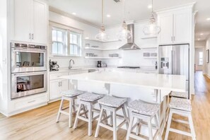 A modern kitchen with white cabinetry, stainless steel appliances, and a large island with bar stools. - Beach Vista Two Beach House (Orange Beach)