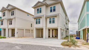 A row of two-story townhouses with garage doors, a paved driveway, and a grassy area with a dune. - Beach Vista Two Beach House (Orange Beach)