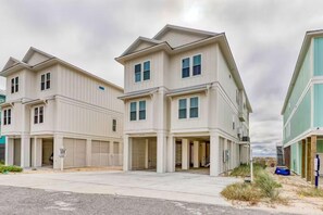 A row of two-story townhouses with garage doors, a paved driveway, and a grassy area with a dune. - Beach Vista Two Beach House (Orange Beach)