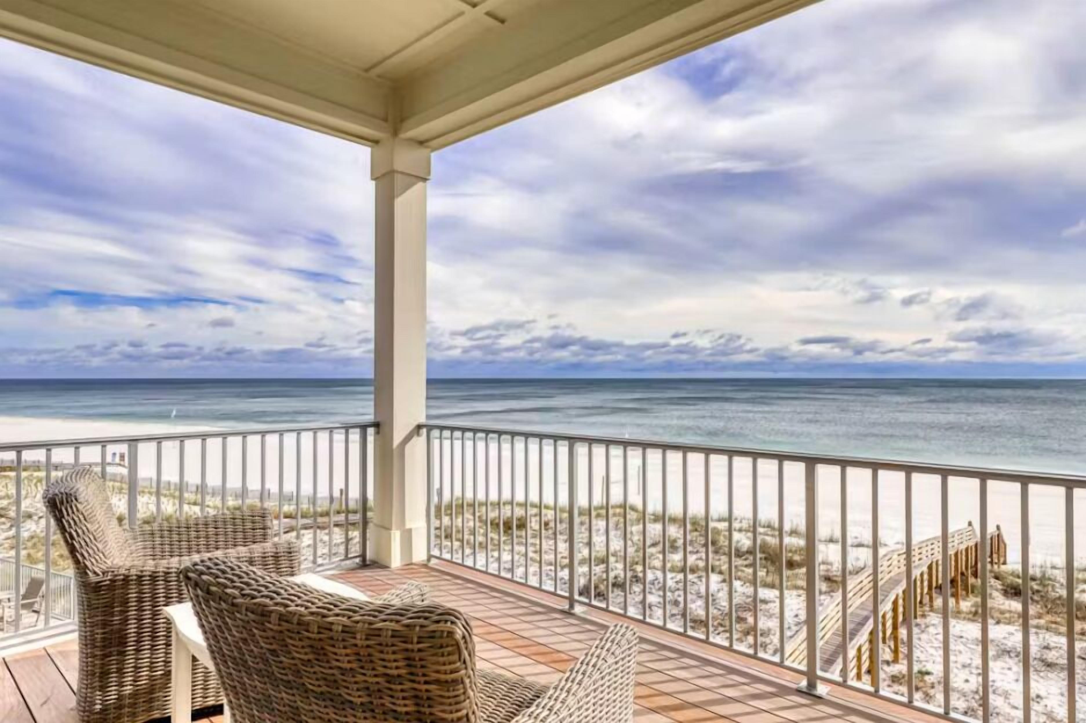 A covered outdoor area with wicker furniture and a view of the beach and ocean.