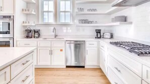 A modern kitchen with white cabinetry, a stainless steel dishwasher, and a gas stove. - Beach Vista Two Beach House (Orange Beach)