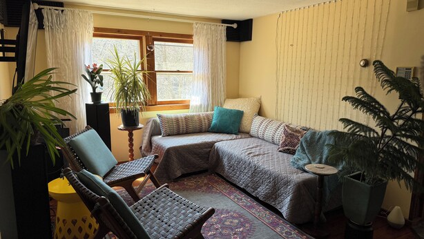 A cozy room with a bed, two chairs, a small table, and a potted plant.