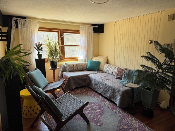 A cozy room with a bed, two chairs, a small table, and a potted plant.