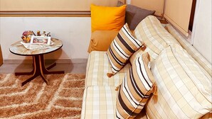 Un espacio habitable compacto con un sofá, almohadas, una pequeña mesa redonda y un estante a cuadros.
