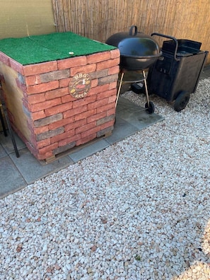 Un espace barbecue en briques, surmonté d’une pelouse verte, avec un gril noir et une brouette.