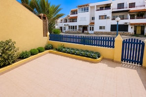 A courtyard with a blue fence, a yellow wall, and a row of green plants.