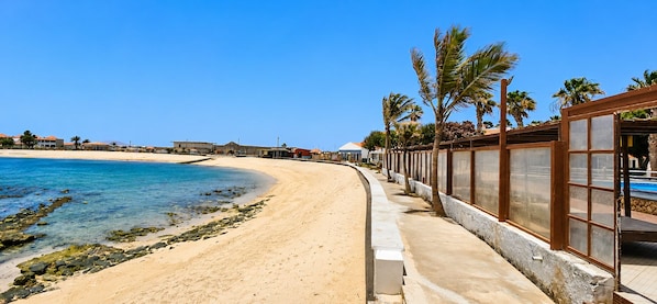A beachside hotel with a curved shoreline, palm trees, and a clear blue sky.