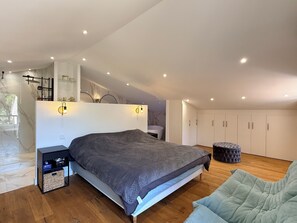 A modern bedroom with a large bed, a nightstand, a seating area, and a wardrobe. - Spacious 2-bedroom apartment, near the golf courses and 10 minutes from the beach (Saint-Raphaël)