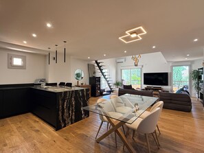 A modern living space with a glass dining table, a black kitchen island, a staircase, and a TV in the living area. - Spacious 2-bedroom apartment, near the golf courses and 10 minutes from the beach (Saint-Raphaël)
