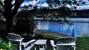 En vacker plats vid sjön med Adirondack-stolar och ett picknickbord, omgiven av grönska och med utsikt över sjön.