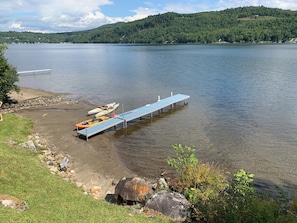 Une jetée au bord du lac, avec des kayaks et un petit bateau, entourée d’une zone herbeuse et, au loin, d’une colline boisée.