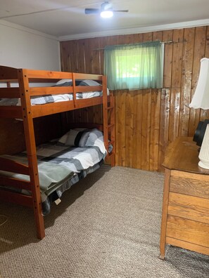 A bunk bed with a wooden frame, a small desk with a lamp, and a window with a green curtain.