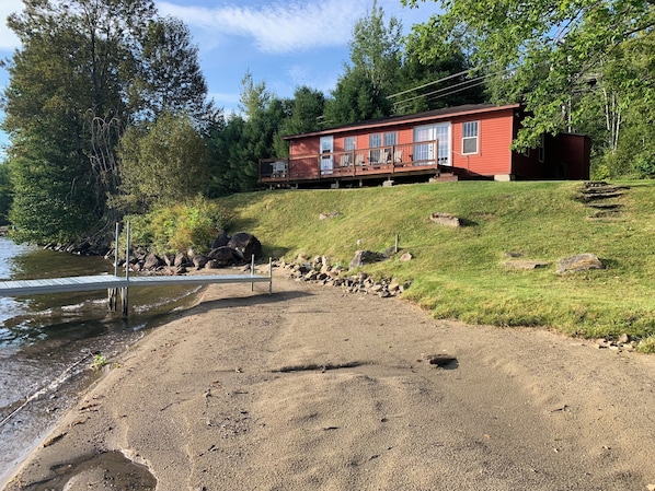 Une cabane rouge avec une terrasse, située sur une colline verdoyante, au bord d’un lac.