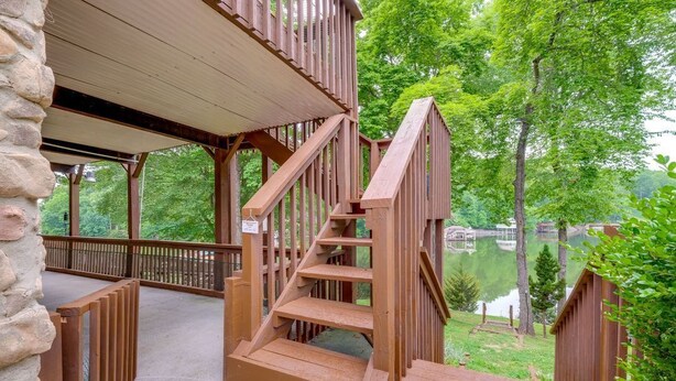 A wooden staircase leading to a covered deck with a view of a lake and trees. - Spacious Waterfront Home on Smith Mountain Lake (Moneta)