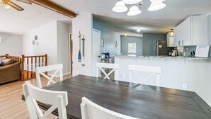 A dining area with a wooden table and white chairs, a kitchen in the background, and a ceiling fan. - Spacious Waterfront Home on Smith Mountain Lake (Moneta)