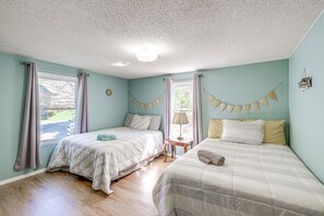 A room with two beds, a window with curtains, a small table with a lamp, and a wall decoration. - Spacious Waterfront Home on Smith Mountain Lake (Moneta)