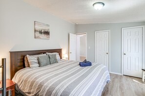 A bedroom with a large bed, a nightstand, a desk, and a door. - Spacious Waterfront Home on Smith Mountain Lake (Moneta)