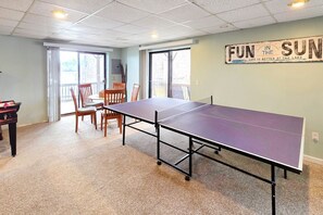 A room with a ping pong table, chairs, a pool table, and a sign on the wall.