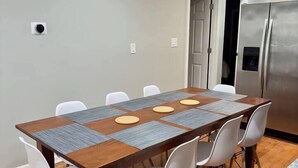 A dining area with a rectangular table surrounded by white chairs, a wooden floor, and a stainless steel refrigerator in the background. - 4BR Downtown Retreat | Free Street Parking (Chicago)