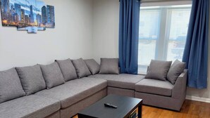 A modern living room with a grey sectional sofa, a small black coffee table, and a cityscape artwork on the wall. - 4BR Downtown Retreat | Free Street Parking (Chicago)