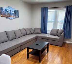 Una sala de estar moderna con un sofá seccional gris, una mesita de centro negra y una obra de arte con un motivo urbano en la pared.