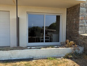 A modern building with a large sliding glass door, a stone wall, and a small garden area. - Appartement plage et vue mer (Quiberon)