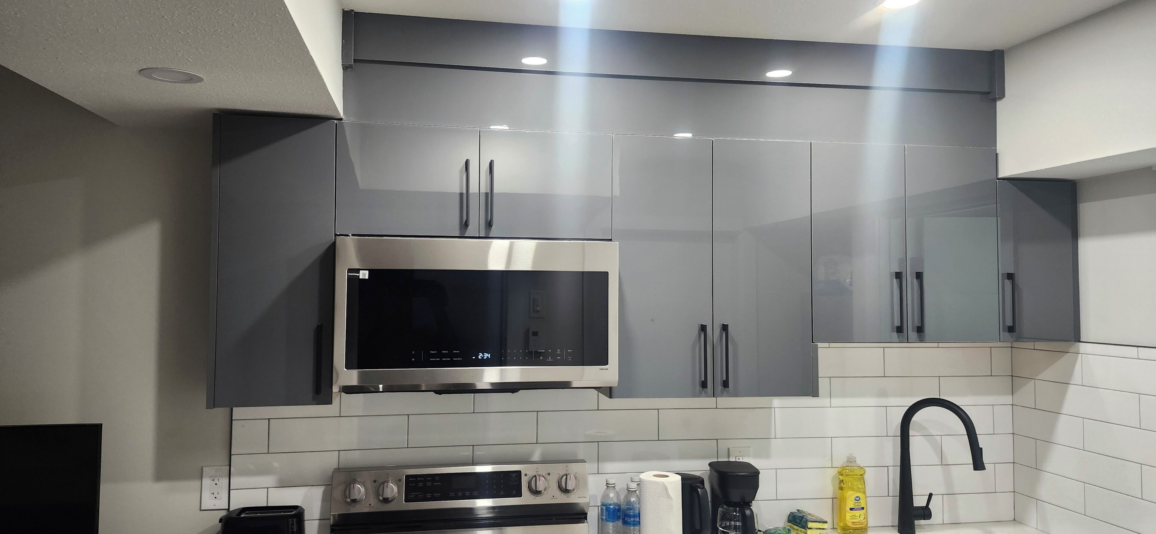 A modern kitchen with stainless steel appliances, grey cabinets, and a tiled backsplash.