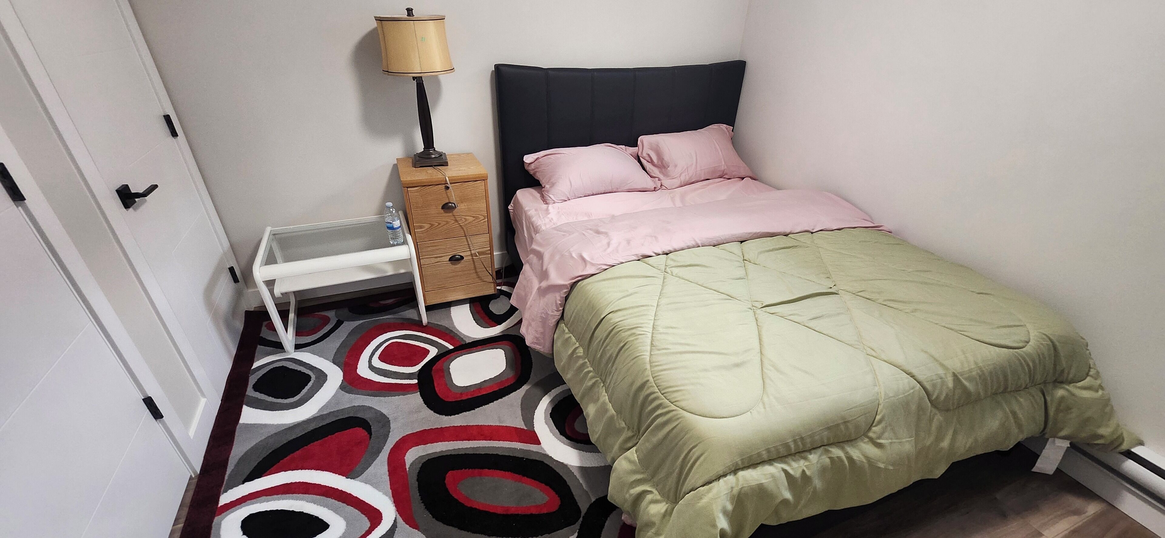 A bedroom with a bed, a bedside table, a lamp, and a rug.