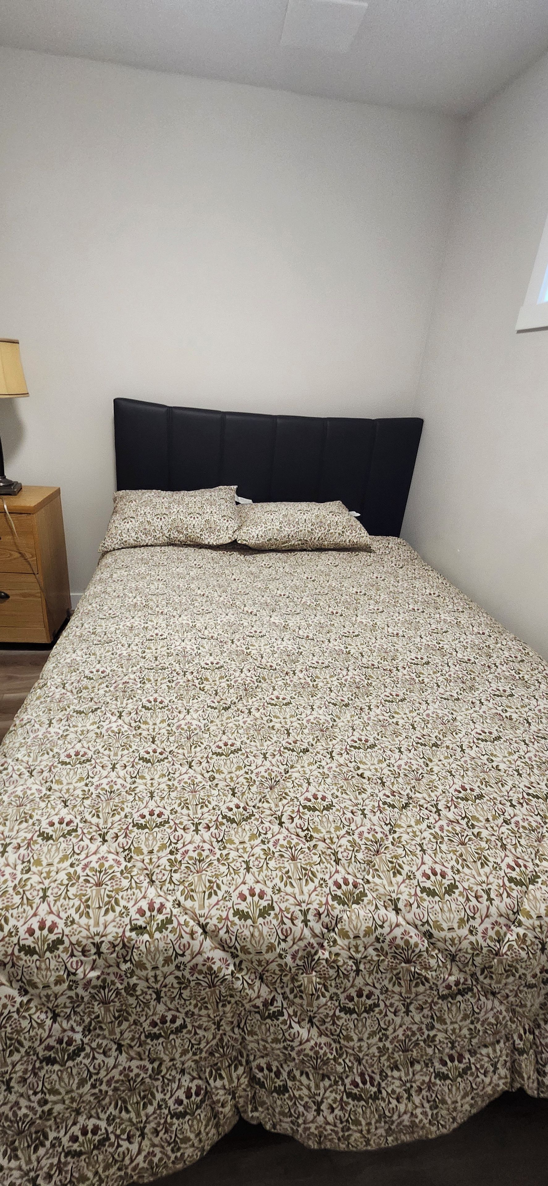 Un lit avec une couvre-lit à motifs floraux, une tête de lit sombre et une table de chevet en bois avec une lampe.