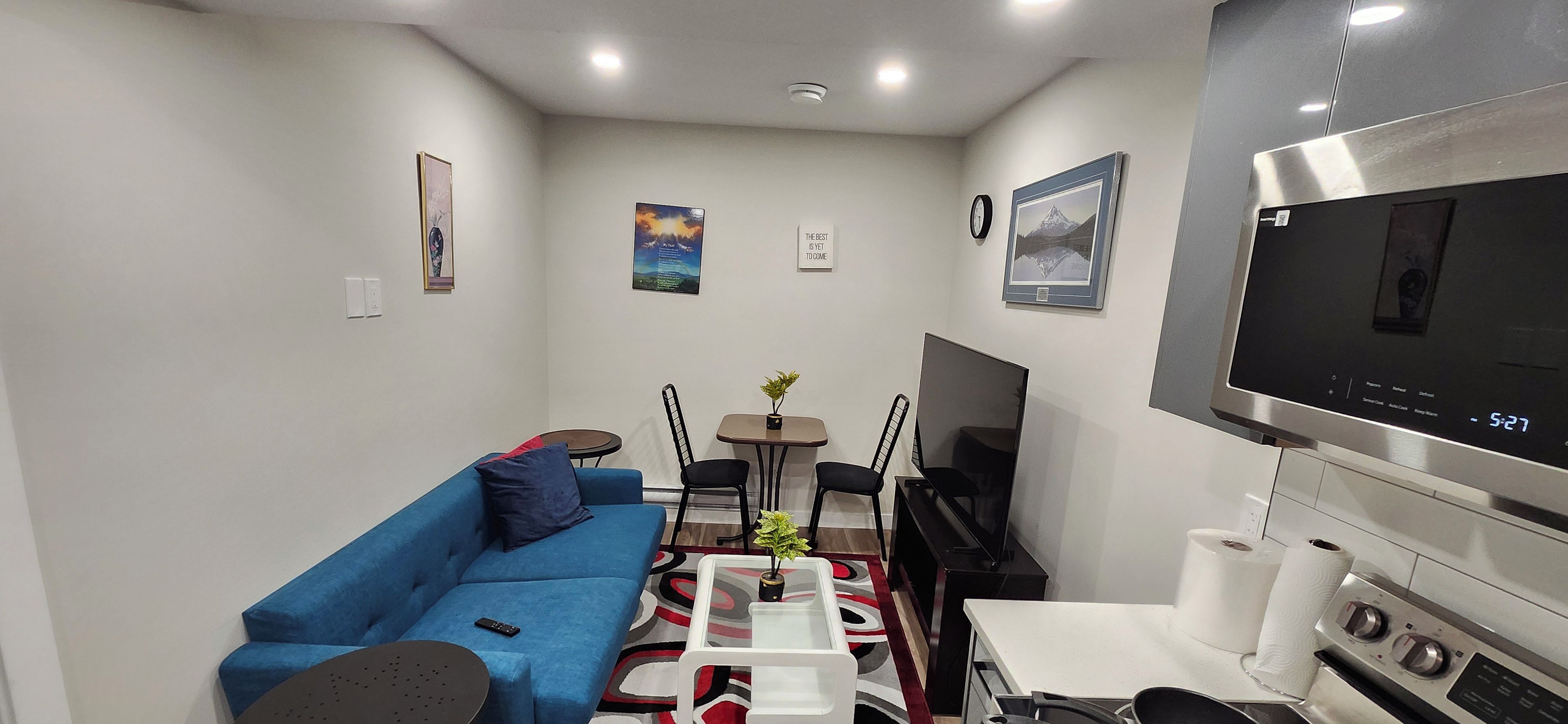 A compact living space with a blue sofa, a small dining table, a TV, and a kitchenette.