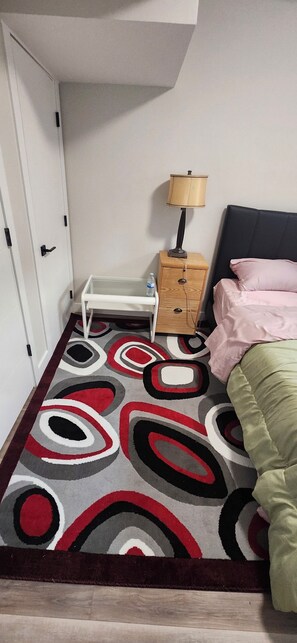Ein Schlafzimmer mit Bett, Nachttisch, Lampe und einem gemusterten Teppich.