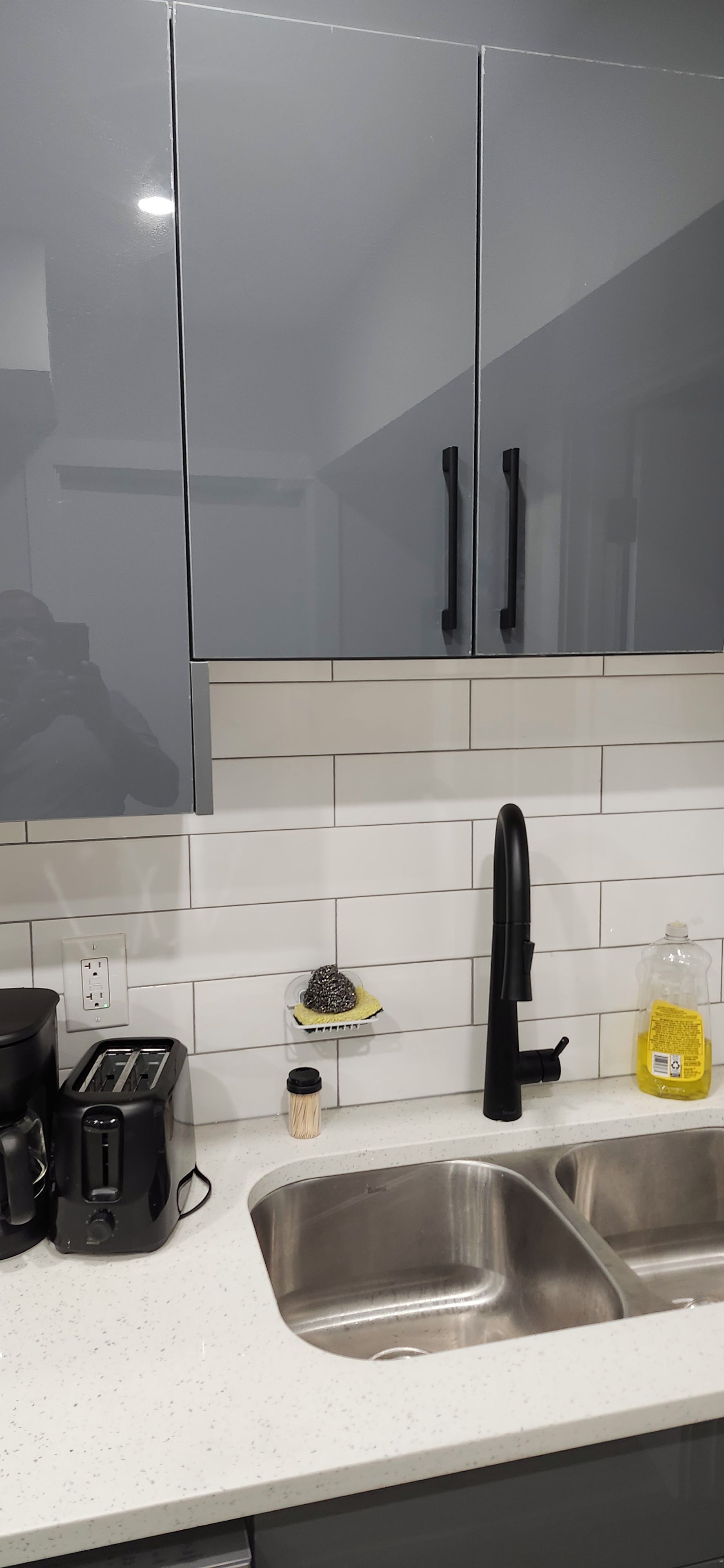 Una cocina con un lavamanos de acero inoxidable, un tostador, una cafetera y un estante para especias.