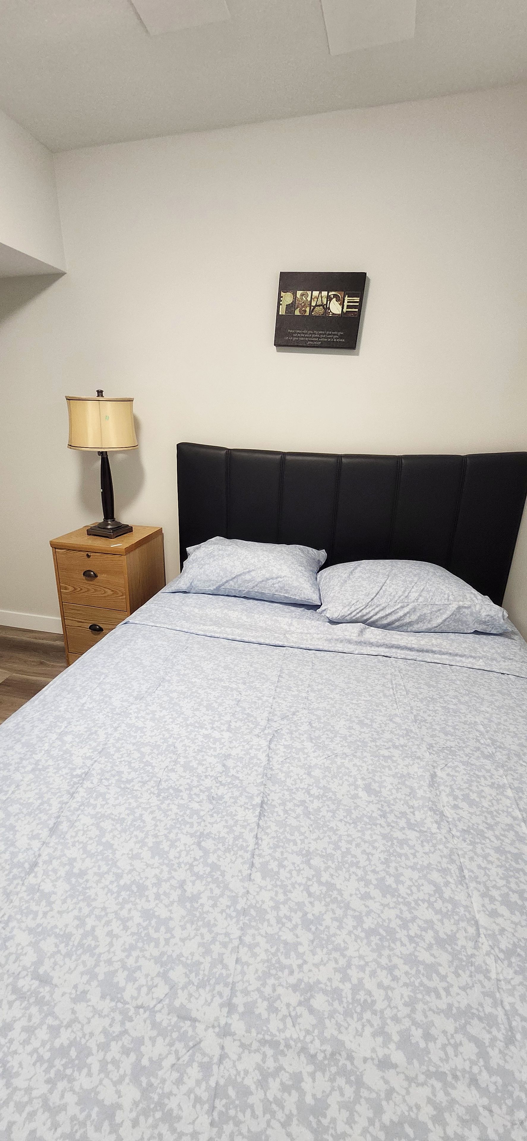 Une chambre à coucher avec un lit, une table de chevet, une lampe et un panneau fixé au mur.