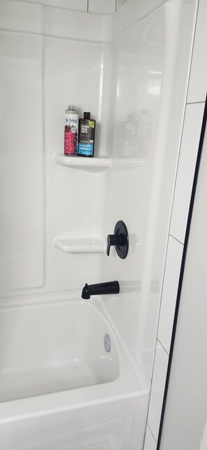 Eine weiße Badewanne mit einem schwarzen Wasserhahn und Ablage für Pflegeprodukte.