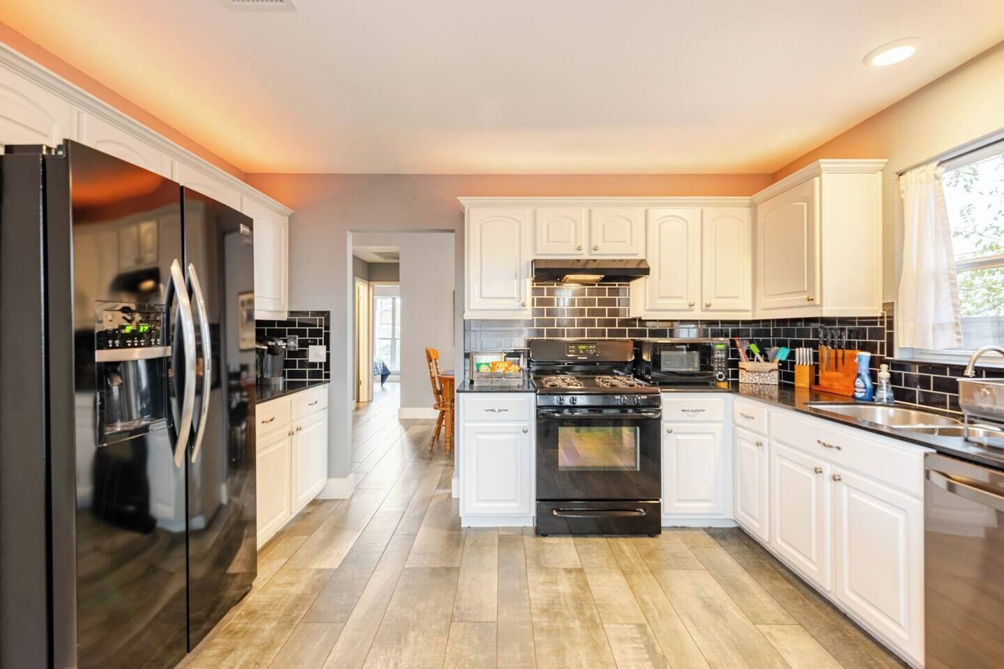 A modern kitchen with white cabinets, a stainless steel refrigerator, a black stove, and a microwave.