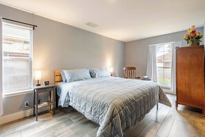 A bedroom with a bed, bedside table, lamp, chair, and a wooden cabinet. - Spacious 3BR · Private Patio · Near Austin (Pflugerville)