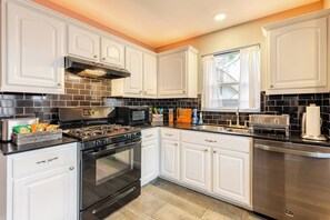 A modern kitchen with white cabinetry, a black tiled backsplash, stainless steel appliances, and a window with curtains. - Spacious 3BR · Private Patio · Near Austin (Pflugerville)