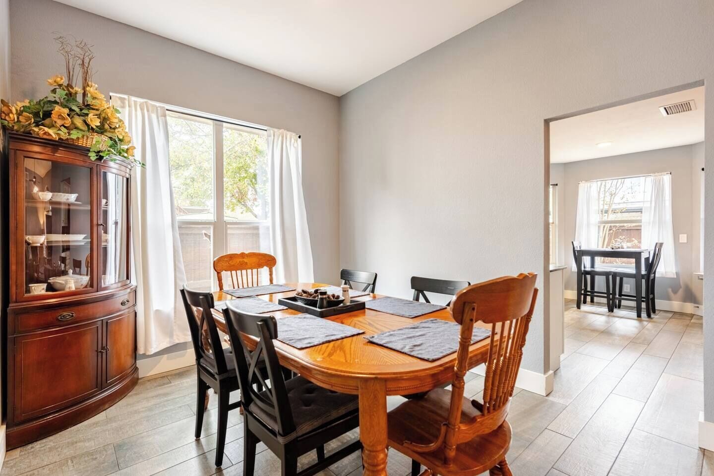 Un coin repas avec une table et des chaises en bois, un meuble avec des portes en verre et une fenêtre avec des rideaux.