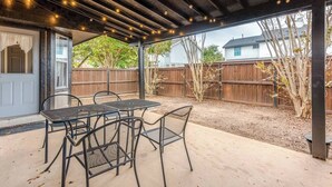 A covered patio area with a table and chairs, a wooden fence, and a view of a house in the background. - Spacious 3BR · Private Patio · Near Austin (Pflugerville)