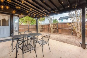 A covered patio area with a table and chairs, a wooden fence, and a view of a house in the background. - Spacious 3BR · Private Patio · Near Austin (Pflugerville)