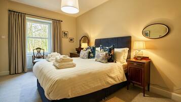 A neatly made bed with a headboard, a bedside table with a lamp, a mirror, and a window with curtains.