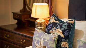 Cama com almofadas decorativas com estampas de pássaros, luminária de cabeceira e mesa de cabeceira de madeira com gavetas.