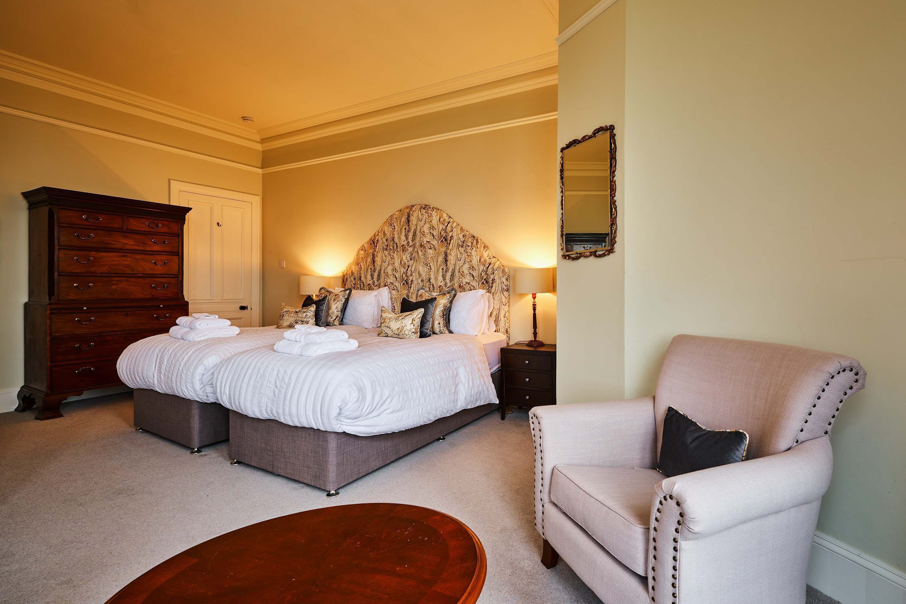 A bedroom with a large bed, a dresser, a chair, and a round coffee table.