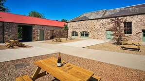 A courtyard with stone buildings, picnic tables, and a bottle of champagne. - Kinclune House Buildings on Private Angus Estate (Kirriemuir)