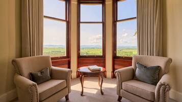 A room with two armchairs, a small table, and a bay window with a view of the countryside.