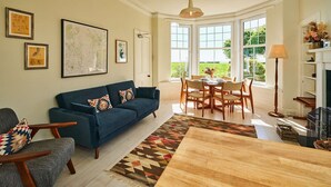 A living room with a blue sofa, a dining table with chairs, a fireplace, and large windows. - Kinclune House Buildings on Private Angus Estate (Kirriemuir)